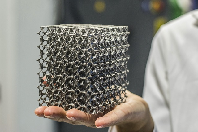 Close-up of a person's hand holding a metal 3D printed lattice structure.