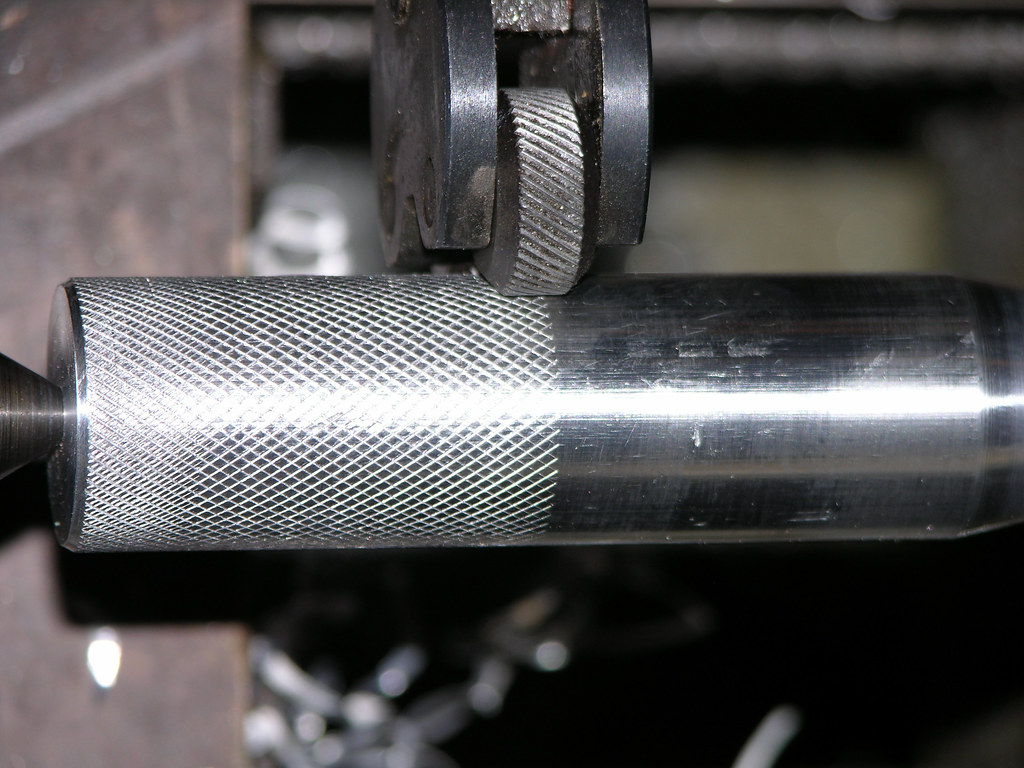 Close-up of a metal rod being knurled on a lathe machine.